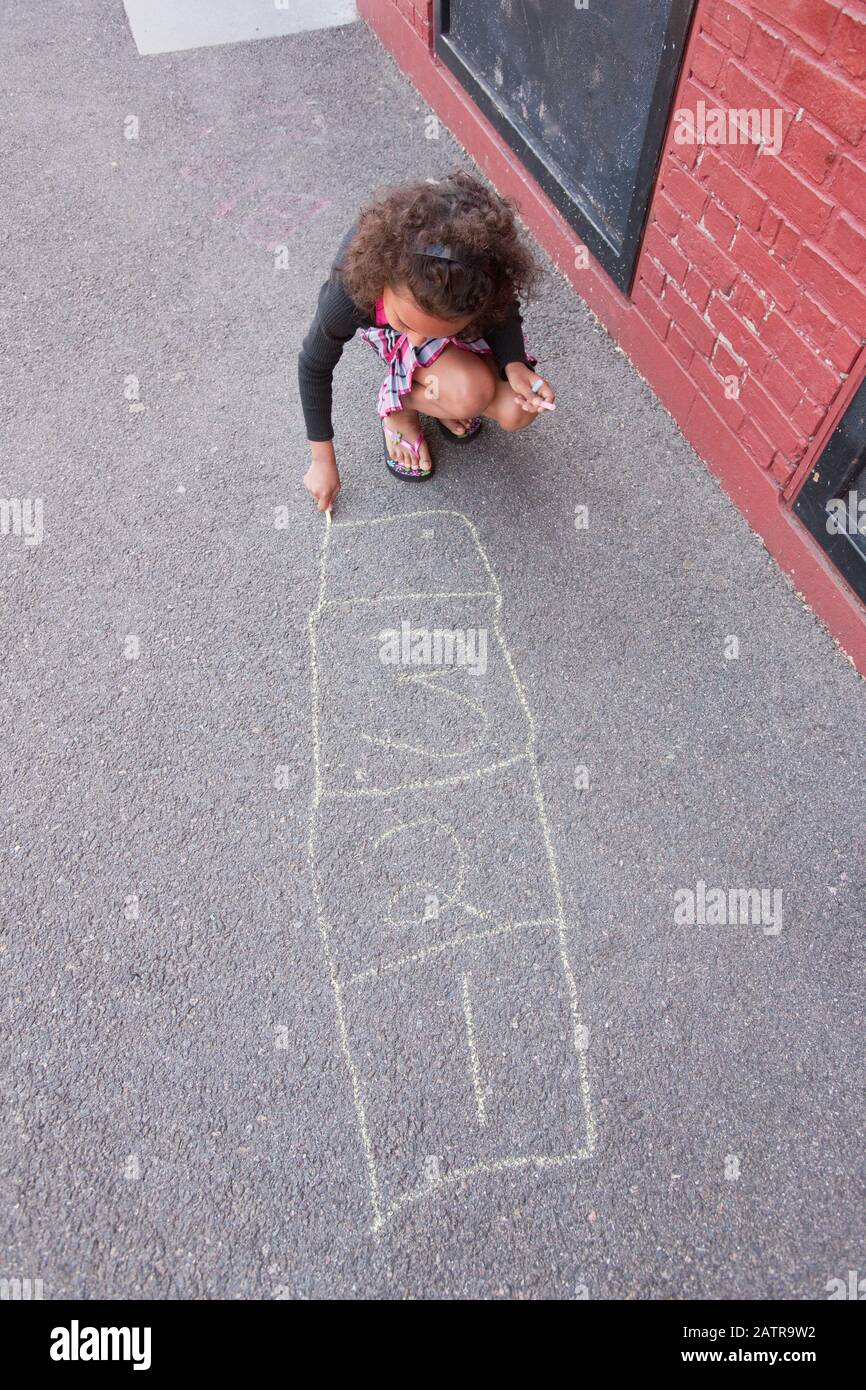 A girl crouches on the sidewalk and draws hopscotch game with chalk Stock Photo