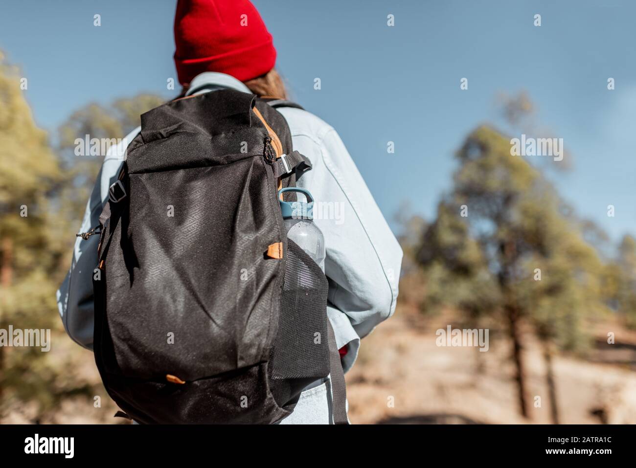 Young woman dressed casually walking with backpack in the forest highly in the mountains on the volcanic rocks Stock Photo