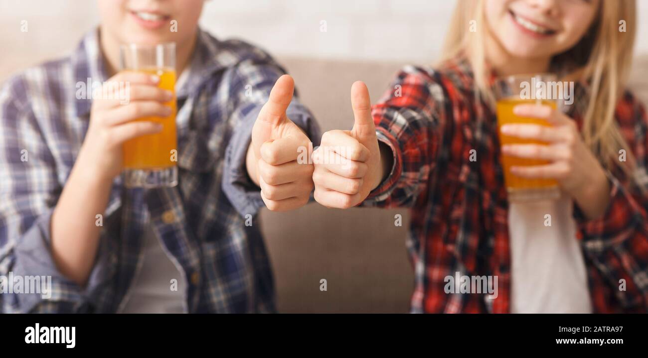 Unrecognizable Brother And Sister Drinking Juice Gesturing Thumbs-Up On Couch Stock Photo