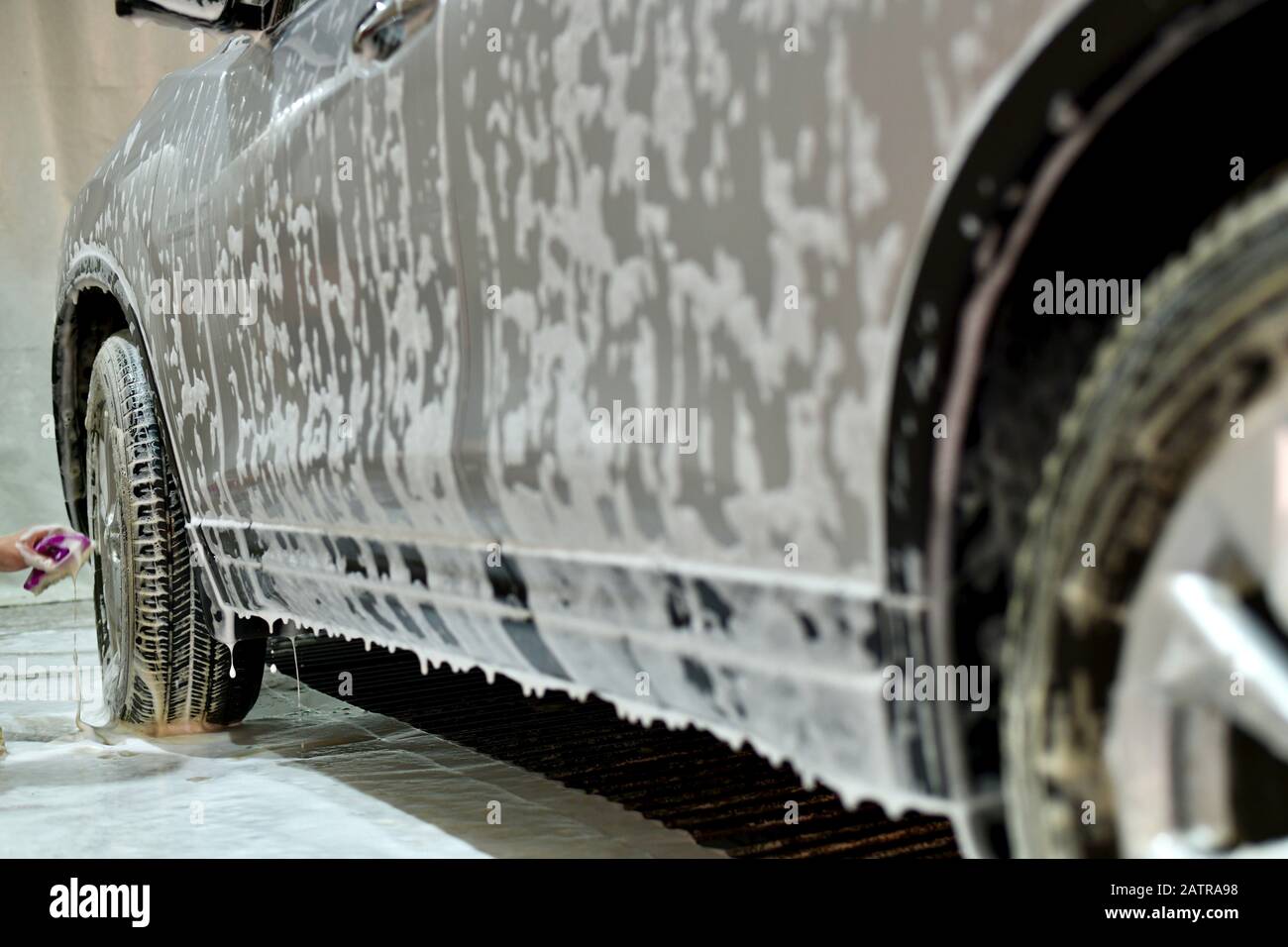 The hand of the worker washes the front wheels with a car with a brush with foam. Stock Photo