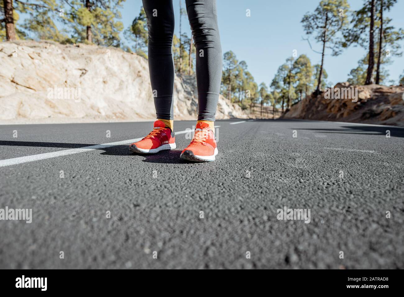 Sports woman in running shoes standing on the asphalt mountain road, closeup on sneakers Stock