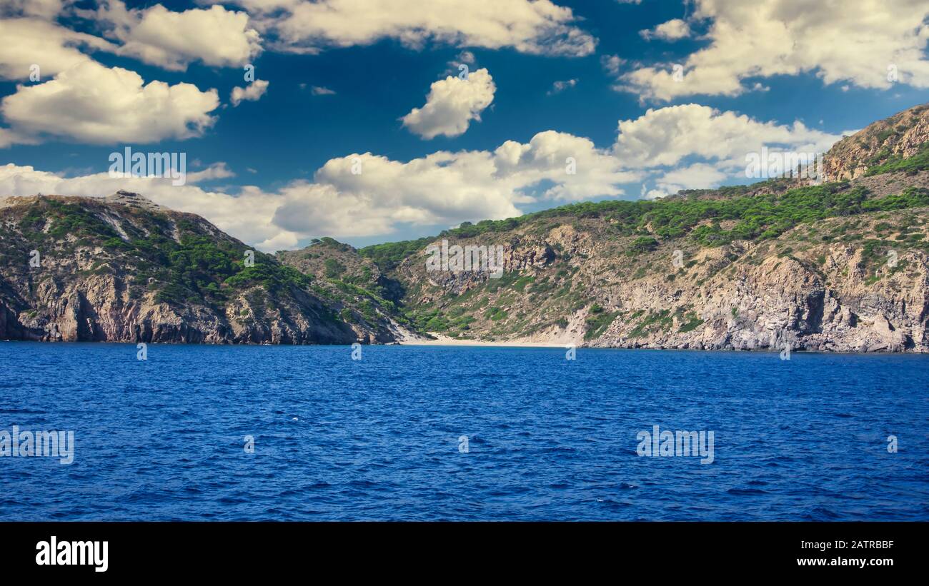 Horizontal photo with view on small beach on small island between famous Greek islands Kos and Nisyros. Sky and sea are blue. Sky is with few clouds. Stock Photo