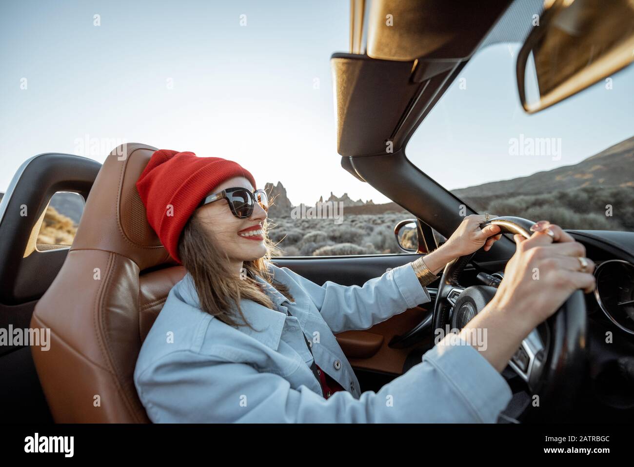 Happy woman in red hat driving convertible car while traveling on the ...
