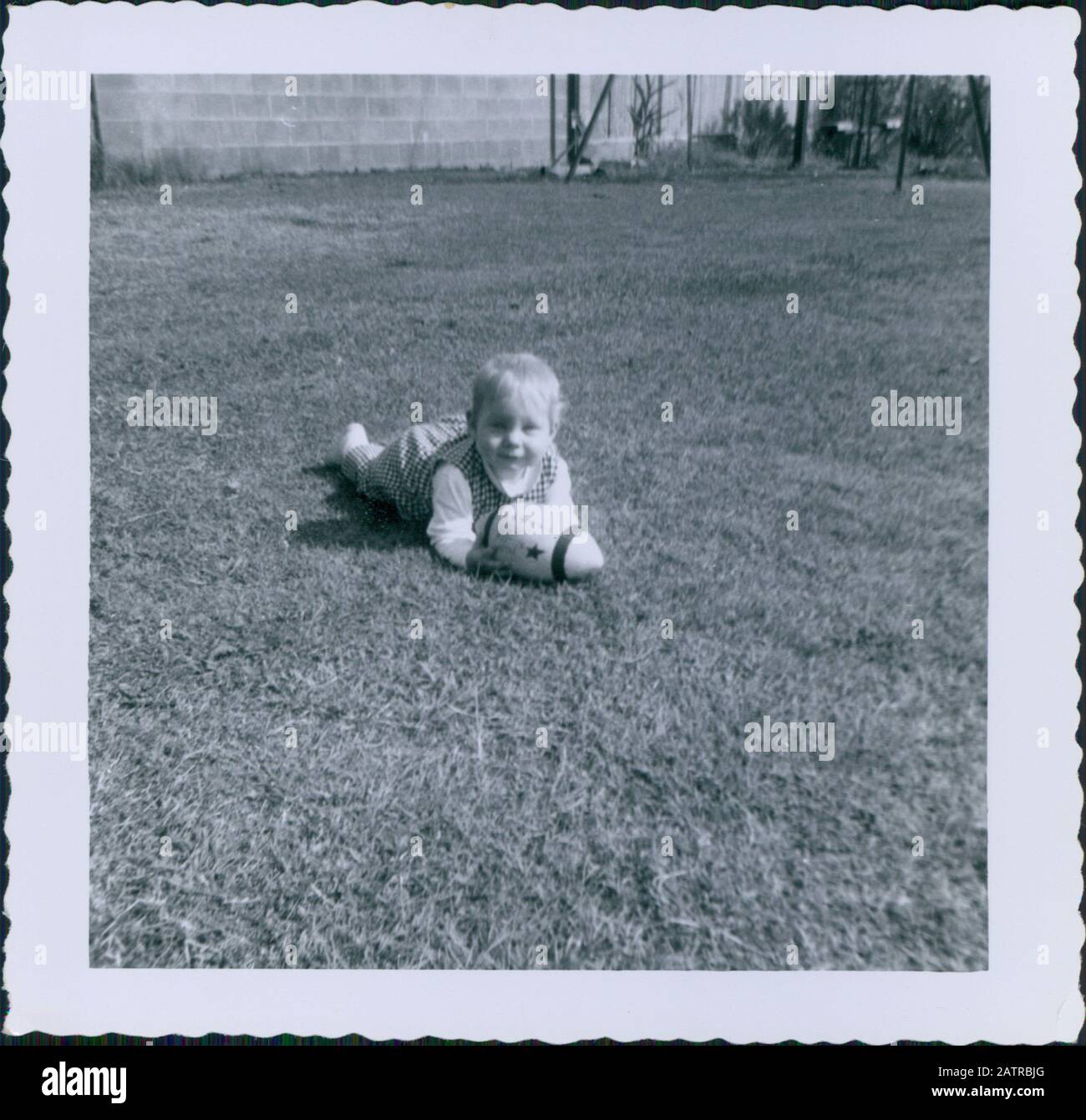 Printed vernacular snapshot image, believed to depict grayscale photo of child lying on grass field with football, 1958. Major topics/objects detected include Photograph and Child. () Stock Photo