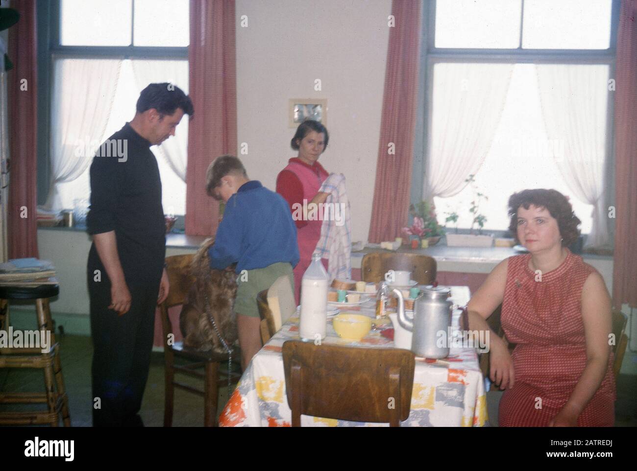 Vernacular photograph taken on a 35mm analog film transparency, believed to depict man in black vest standing beside woman in red and white stripe shirt during a meal at a youth hostel, 1970. Major topics/objects detected include People and Family. () Stock Photo