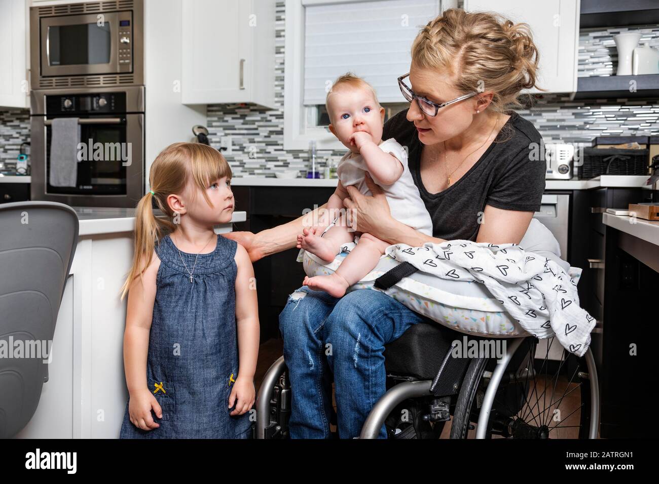 https://c8.alamy.com/comp/2ATRGN1/a-paraplegic-mom-in-a-wheelchair-talking-with-her-daughter-and-holding-her-baby-in-her-lap-while-working-in-her-kitchen-edmonton-alberta-canada-2ATRGN1.jpg