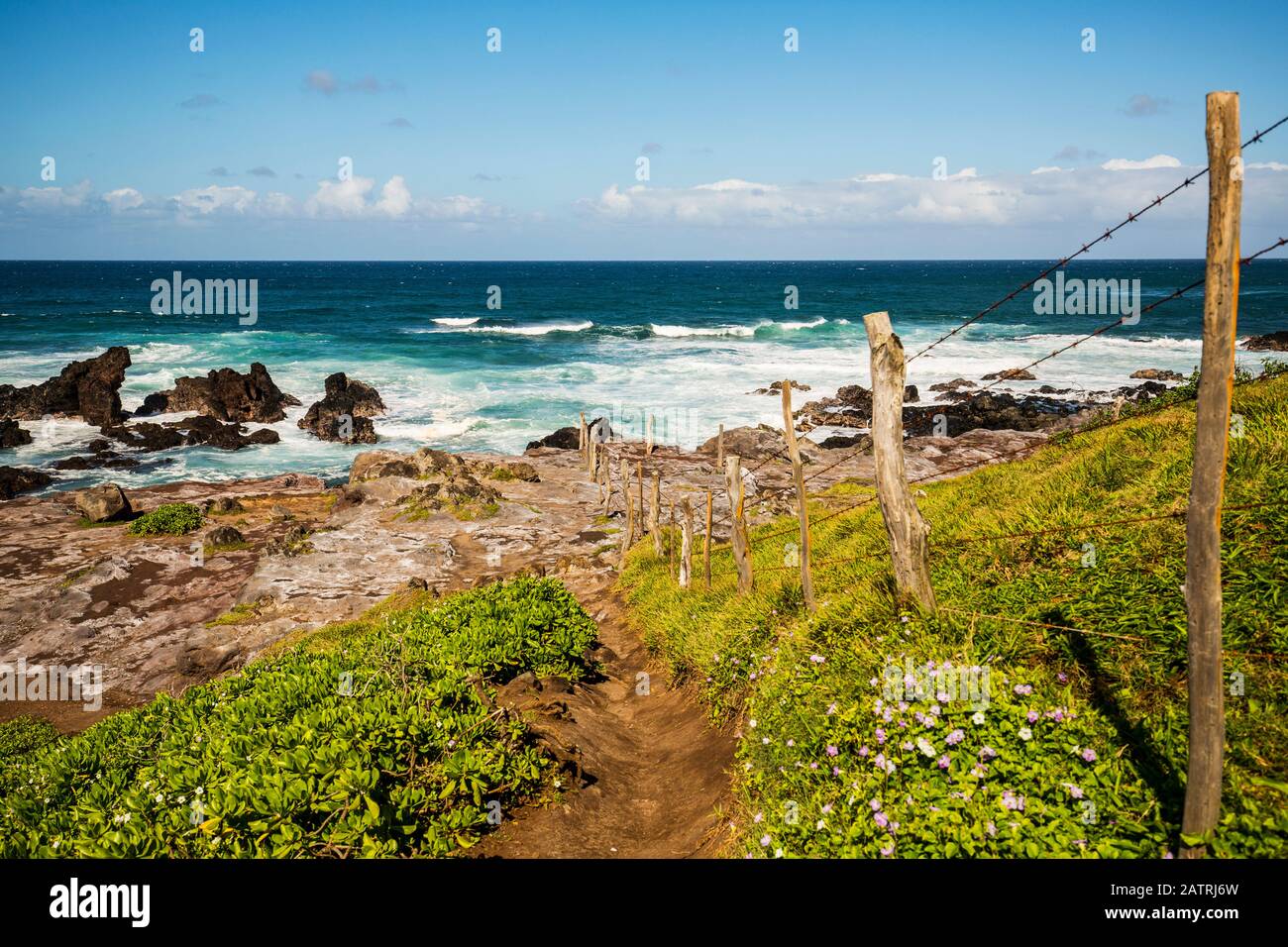Ocean waves cresting and rollling into the rocky shoreline with a dirt path on a fenceline and clouds on the horizon as viewed from the Ho'okipa Lo... Stock Photo