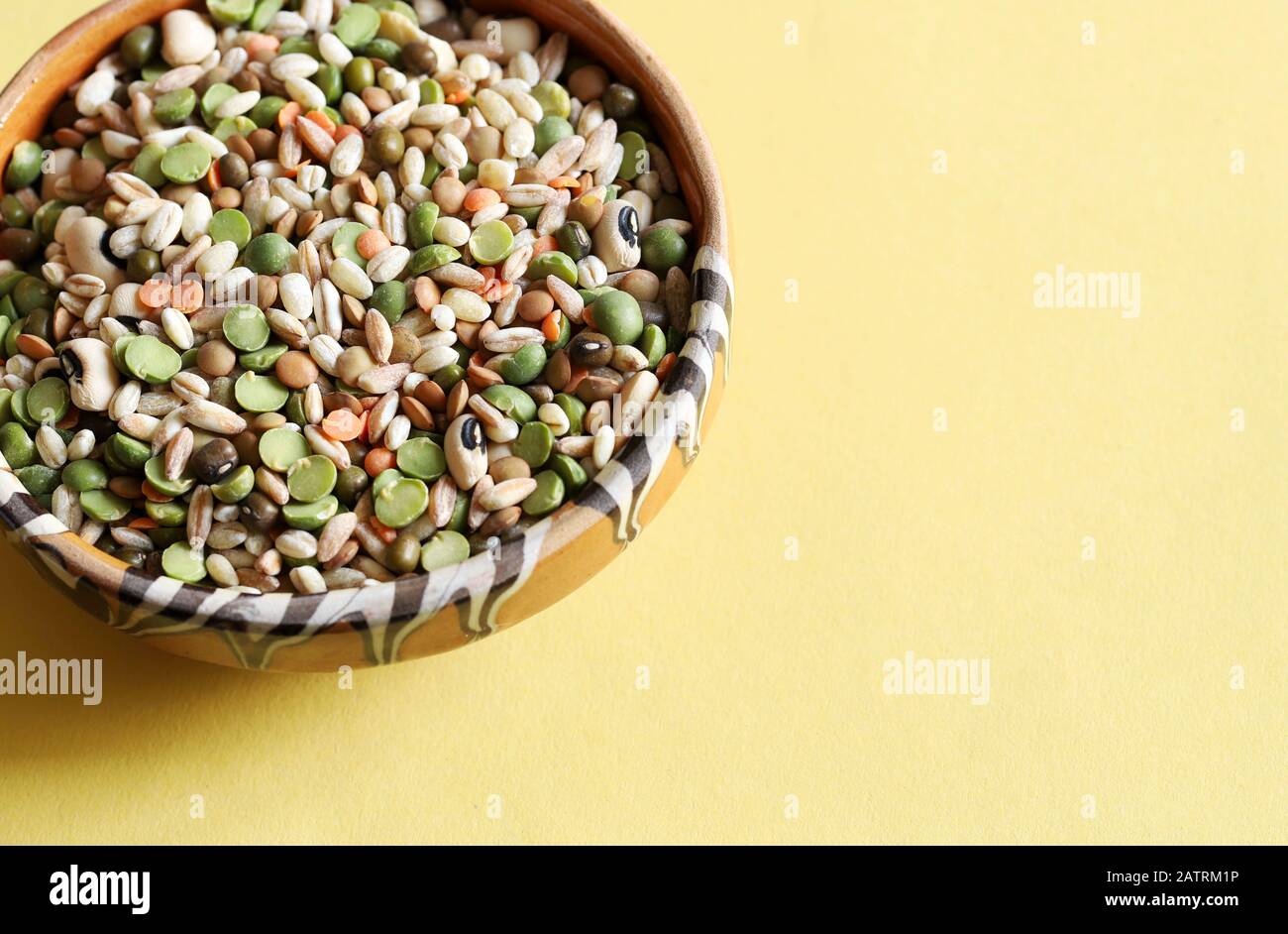 Mixed dried legumes in the bowl isolated on a yellow background.Top view. Stock Photo