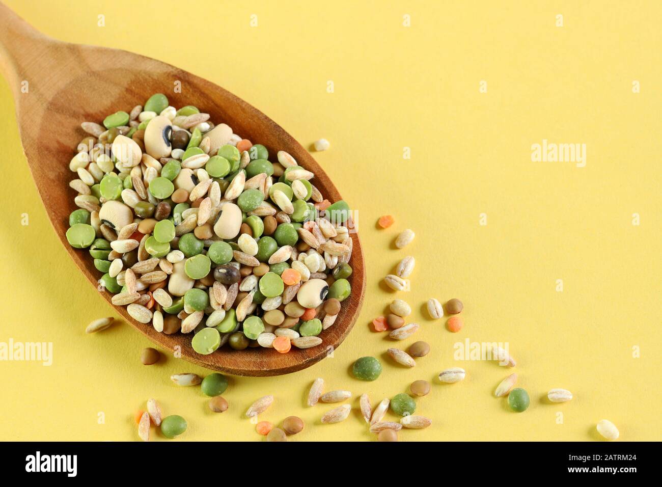 Mix of dried legumes in a wooden spoon isolated on yellow background. Top view. Stock Photo