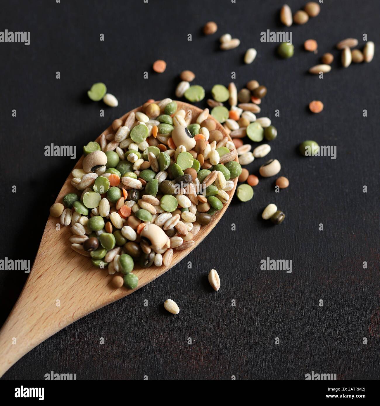 Mix of dried legumes in a wooden spoon isolated on dark background. Top view. Stock Photo