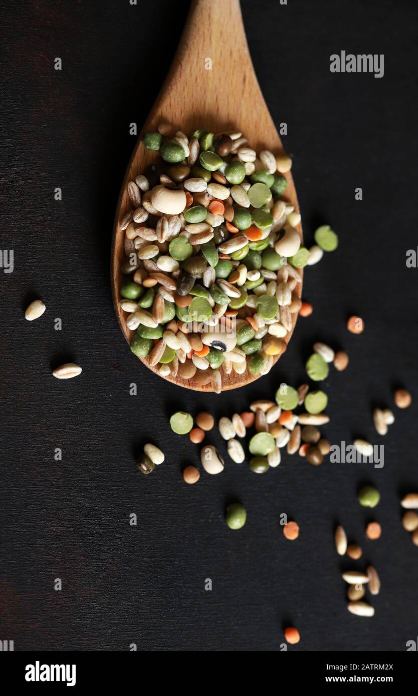Mix of dried legumes in a wooden spoon isolated on dark background. Top view. Stock Photo