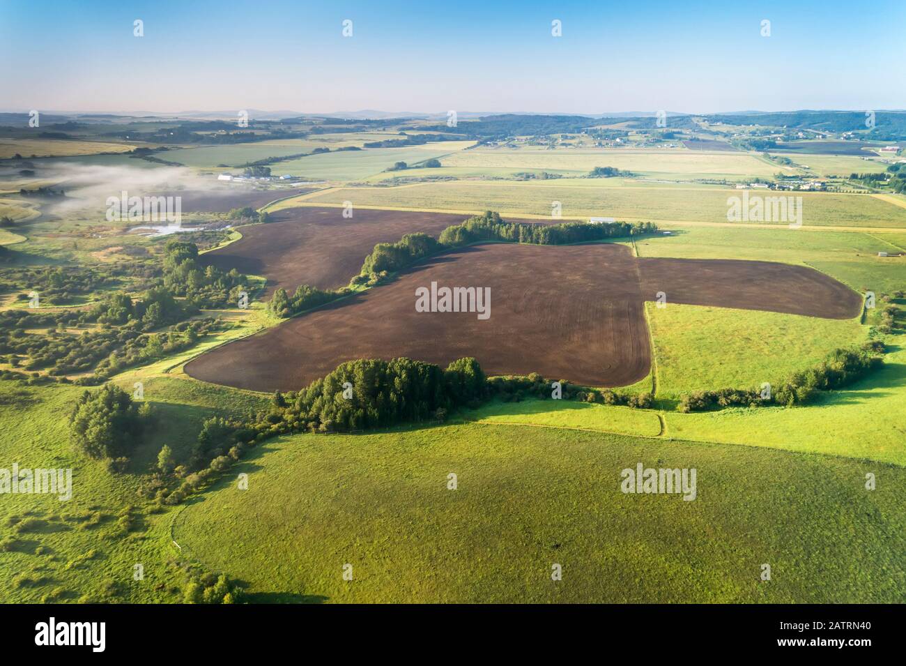 Aerial view of a dark clean soil field surrounded by trees and green fields, West of Calgary; Alberta, Canada Stock Photo