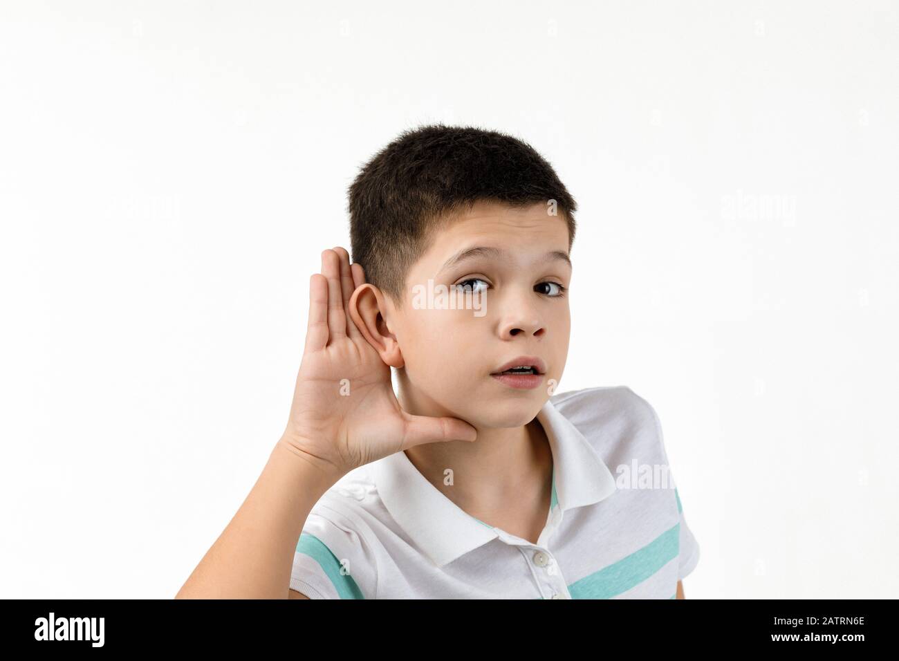 happy little child boy in striped t-shirt making hearing gesture on white background. facial expression. kid with hand over ear listening gossip. Stock Photo