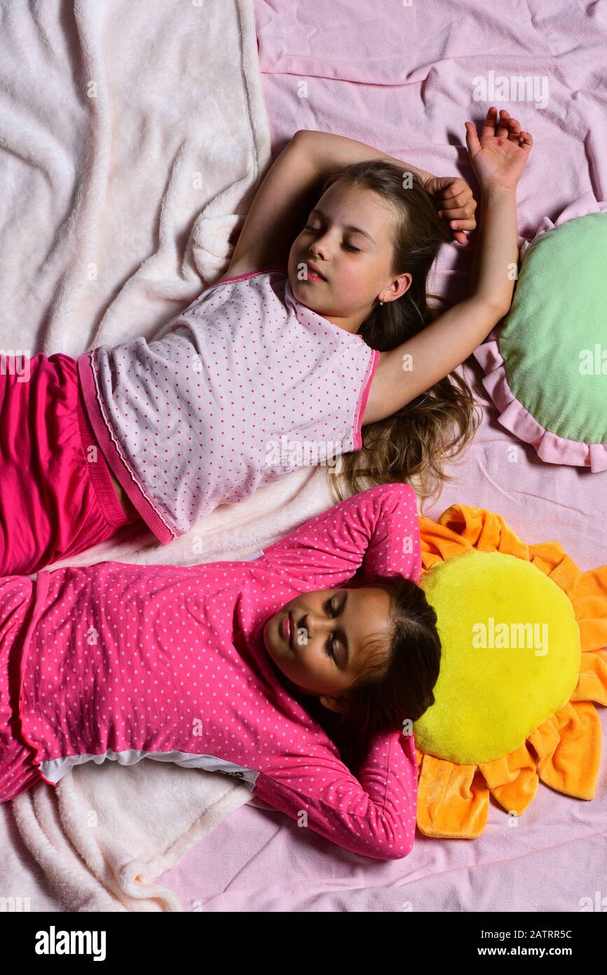 Kids with peaceful faces have rest in bed. Girls lie on white and