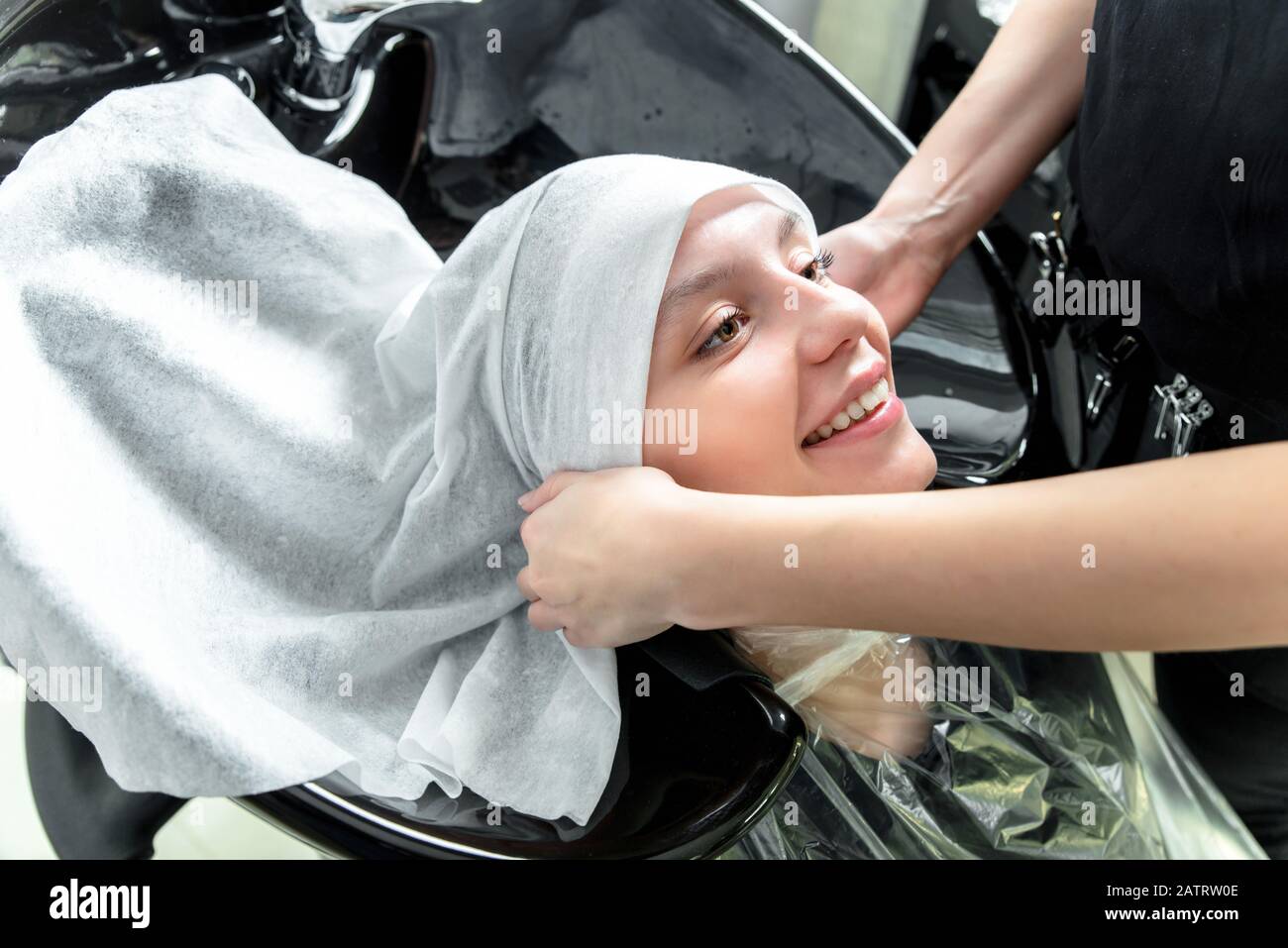 Professional hairdresser drying woman's hair after washing using towel