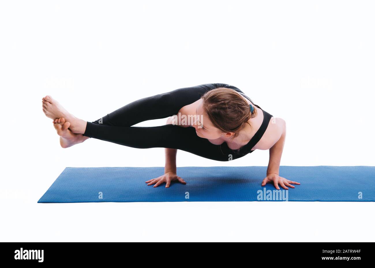 Young woman is doing yoga exercise (parsva bakasana) on blue mat white background. Stock Photo