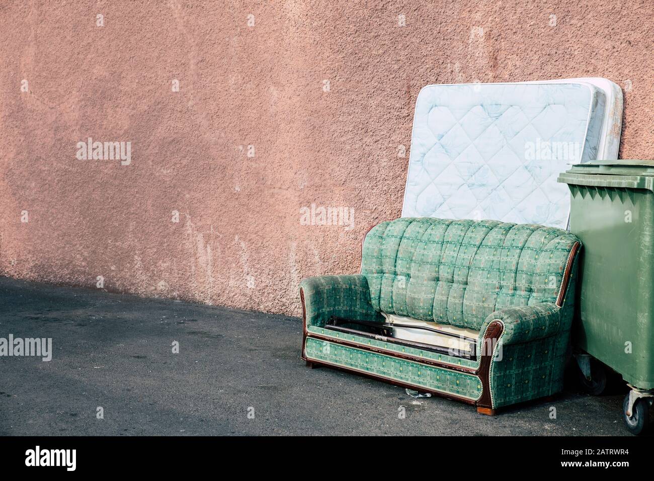 Old sofa and mattress thrown away outdoors by the house building and by the garbage can. A lot of copy space. Stock Photo