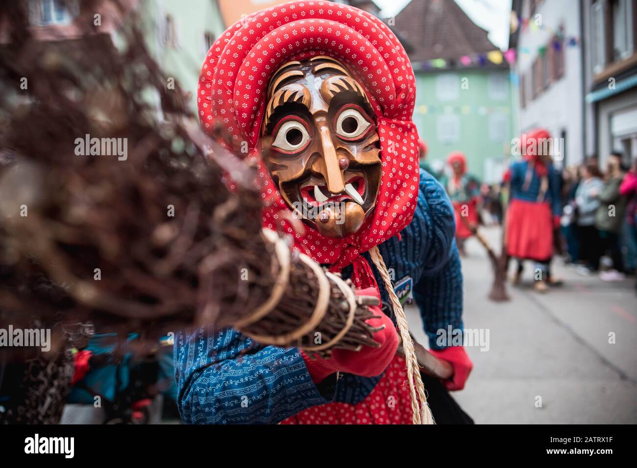 Kandel witch from Waldkirch - funny witch with a red headscarf, lifts up the broom. During the carnival parade in Staufen, southern Germany Stock Photo
