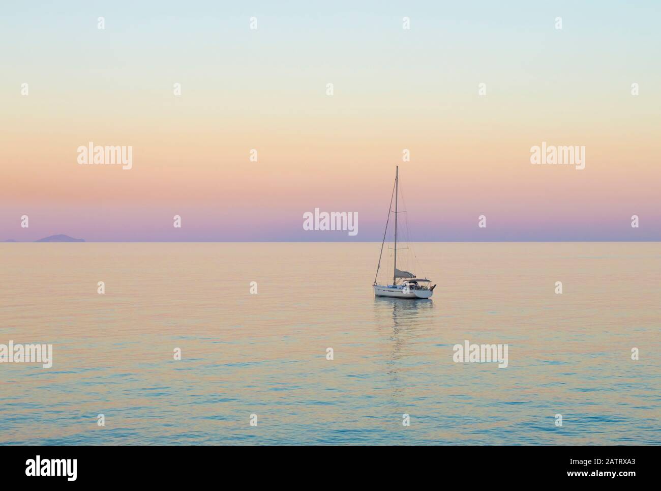 Small white sailboat in Aegean sea by Greek island of Santorini in calm summer evening after sunset. Stock Photo