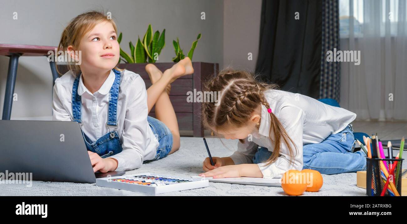Two little sisters lying on the floor at living room and using laptop ...