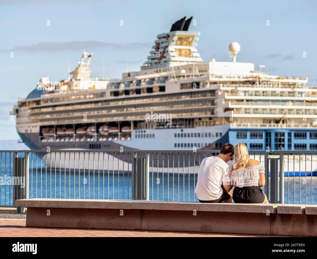 A young couple sit in front of a Cruise Ship berthed in Funchal harbour, Madeira. Stock Photo