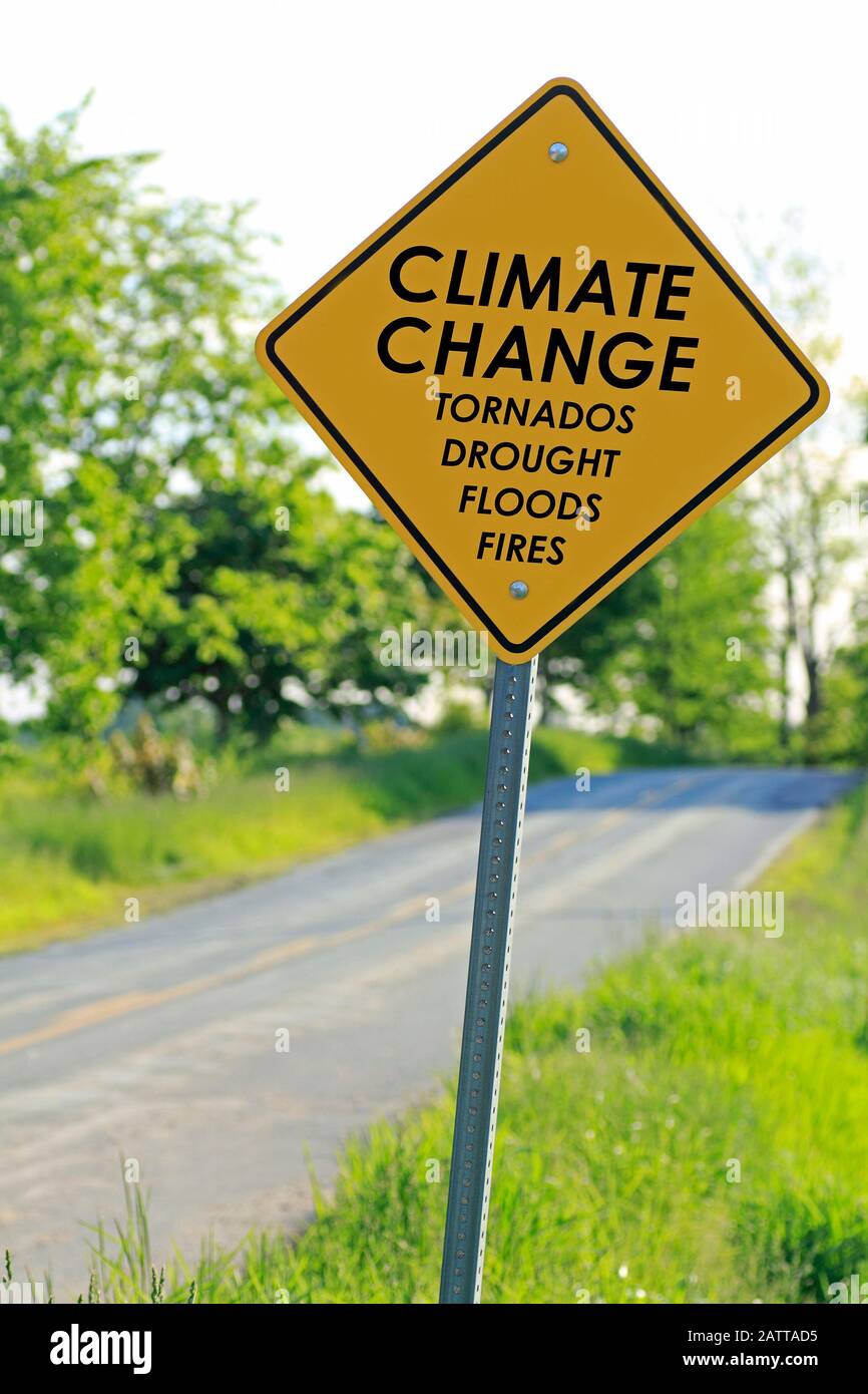 A yellow caution road sign on the side of a highway that says 'Climate Change tornados drought floods fires' as a warning to motorists Stock Photo