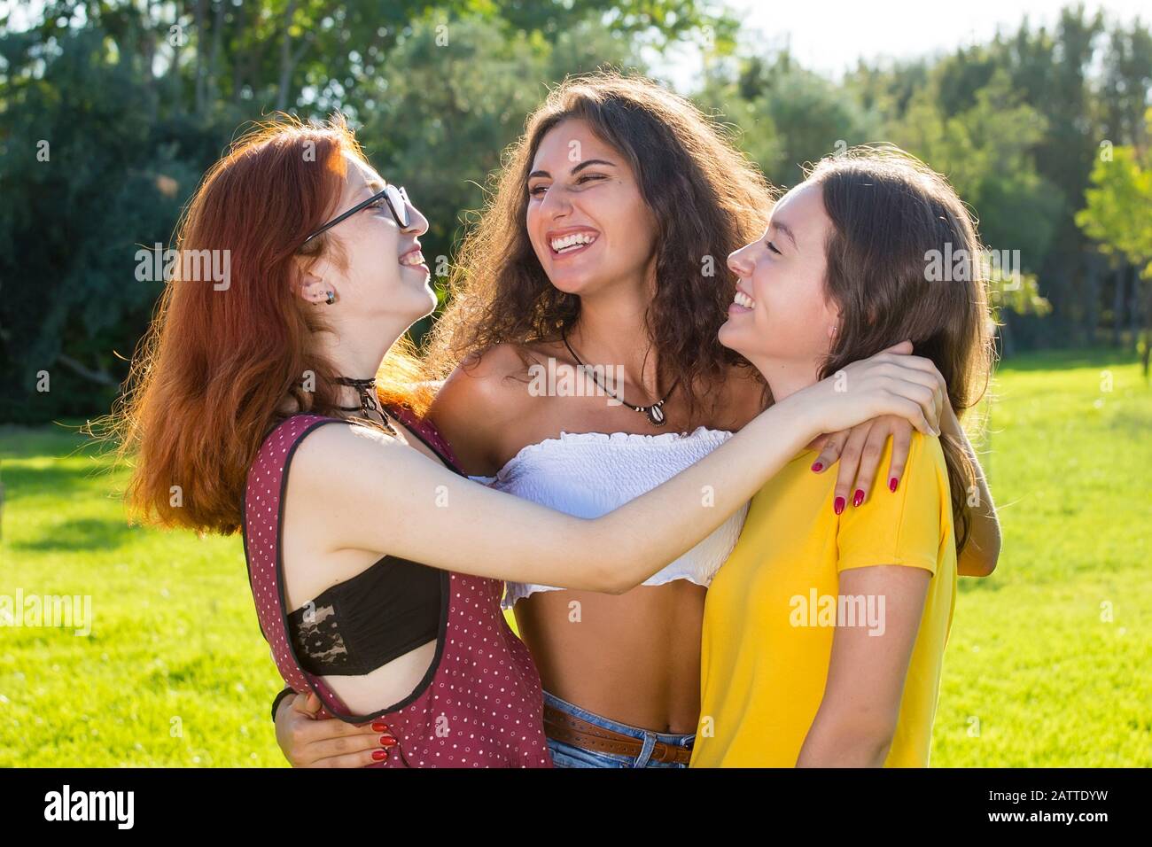 Three girls friends hugging in park and looking at each other with a ...