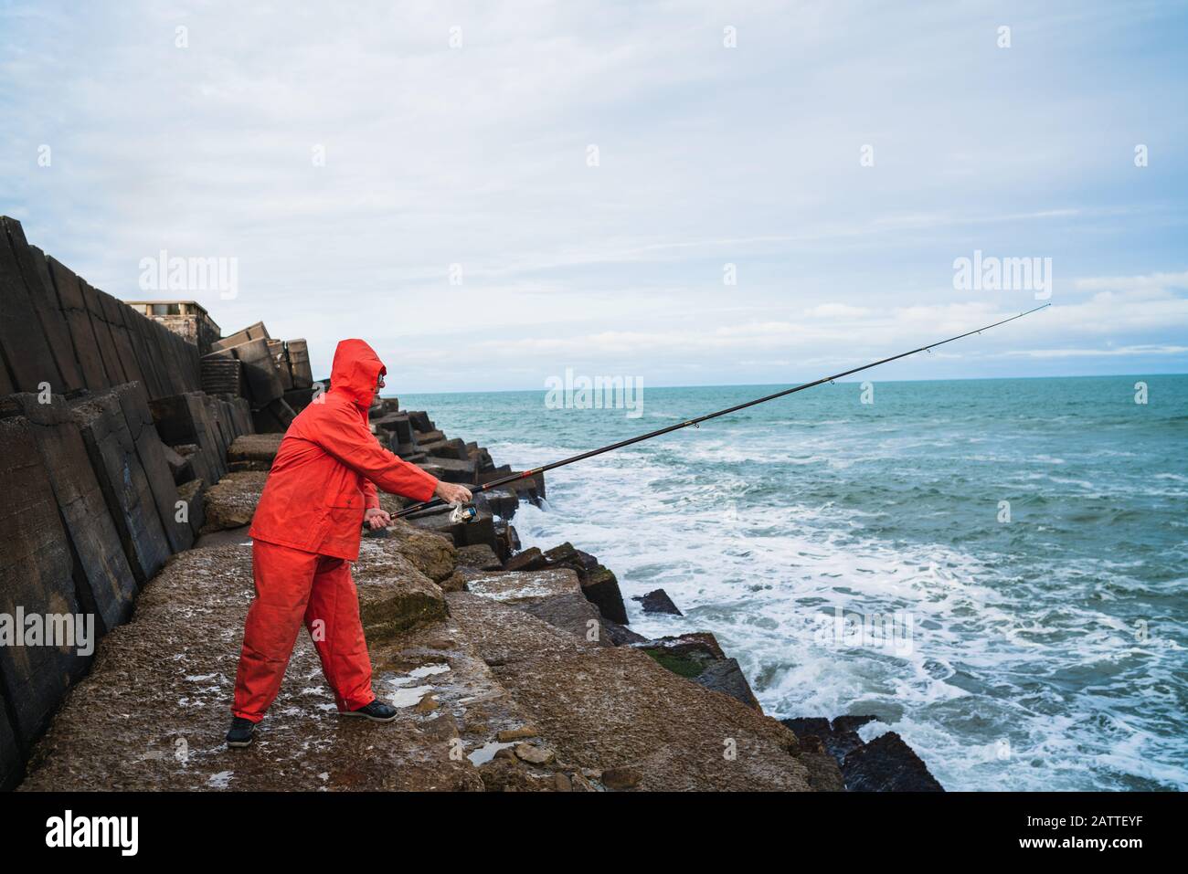 Portrait of an old man fishing on the rocks at the sea. Fishing concept. Stock Photo