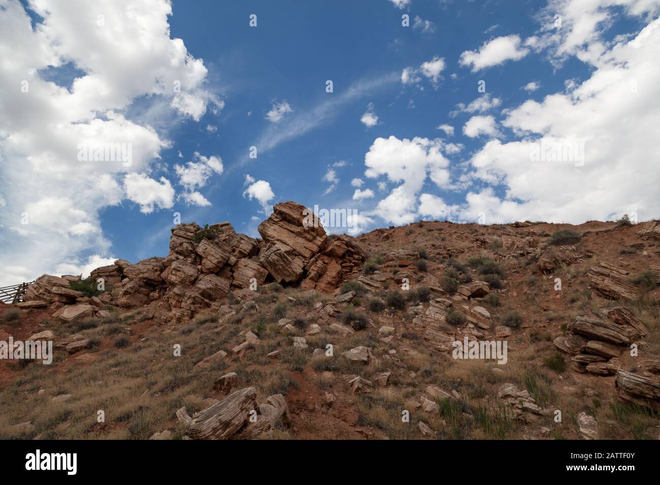 Large stacked boulders seem to defy gravity as they stay perched on the side of a mountain with a blue sky and some white clouds. Stock Photo
