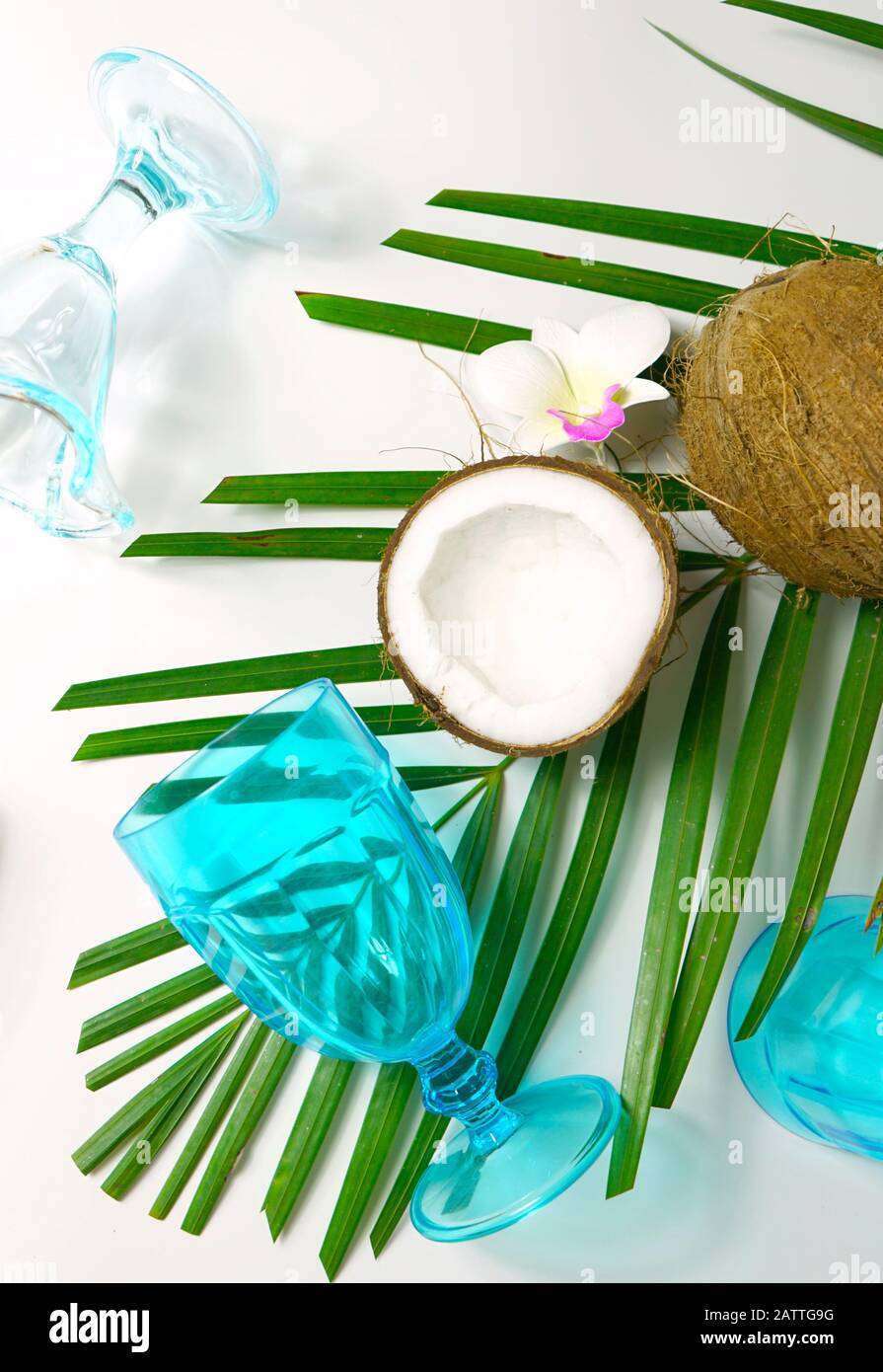 Coconut summertime entertaining theme flat lay creative layout overhead with shadows from blue drinking glasses cast over table. Vertical close up. Stock Photo