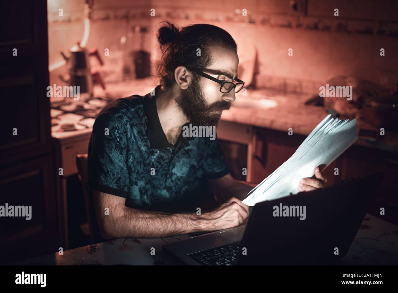 A hipster type young man checking billing information in the kitchen.Subsistence Concept. Stock Photo