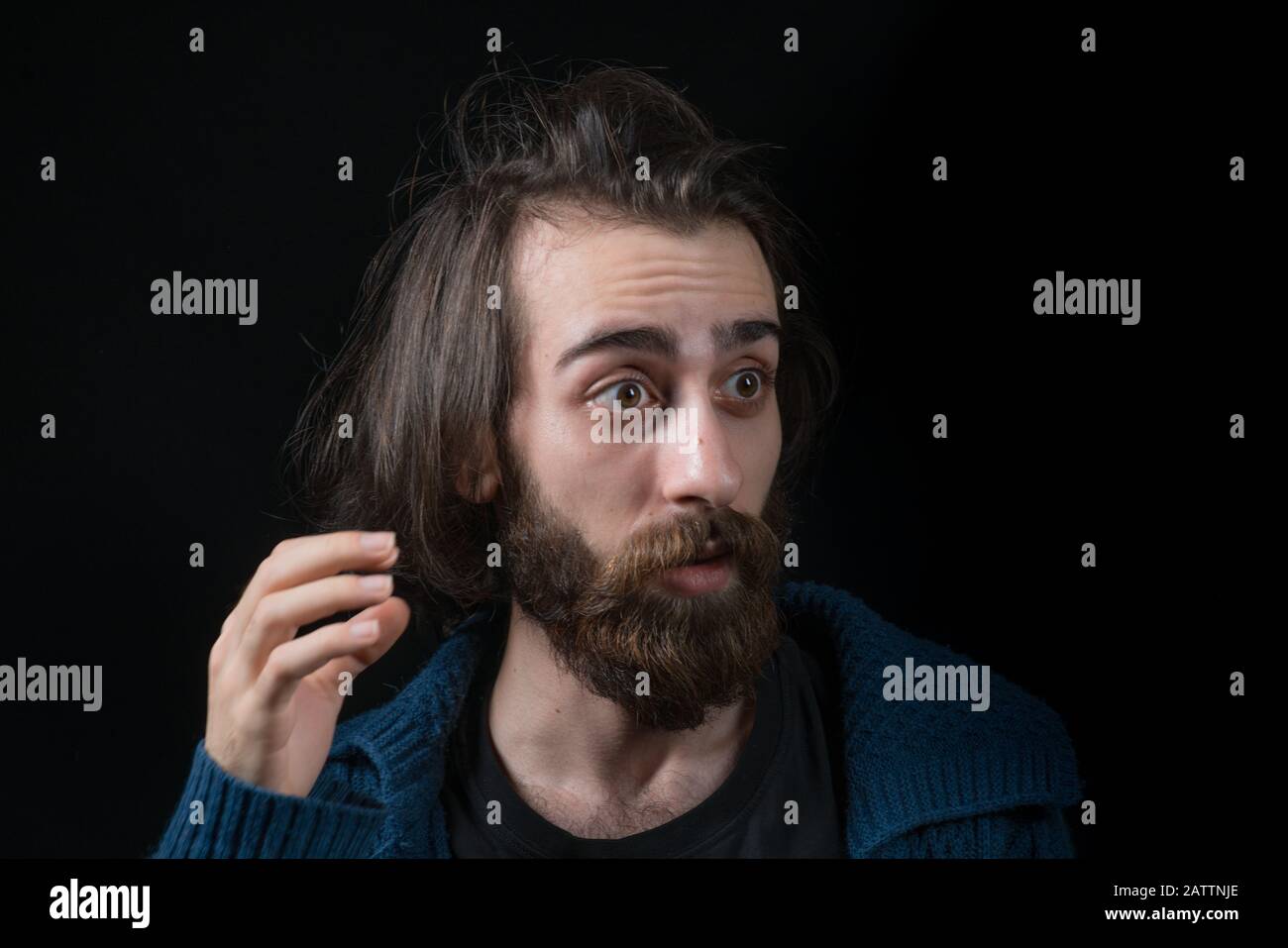 Young man with long hair with hippie type long beard, surprised face, in black isolated background. Hipster Concept. Stock Photo