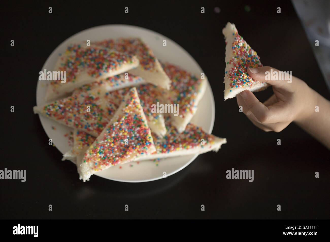 a child taking a piece from a plate of fairy bread, bread buttered and then sprinked with sprinkles Stock Photo