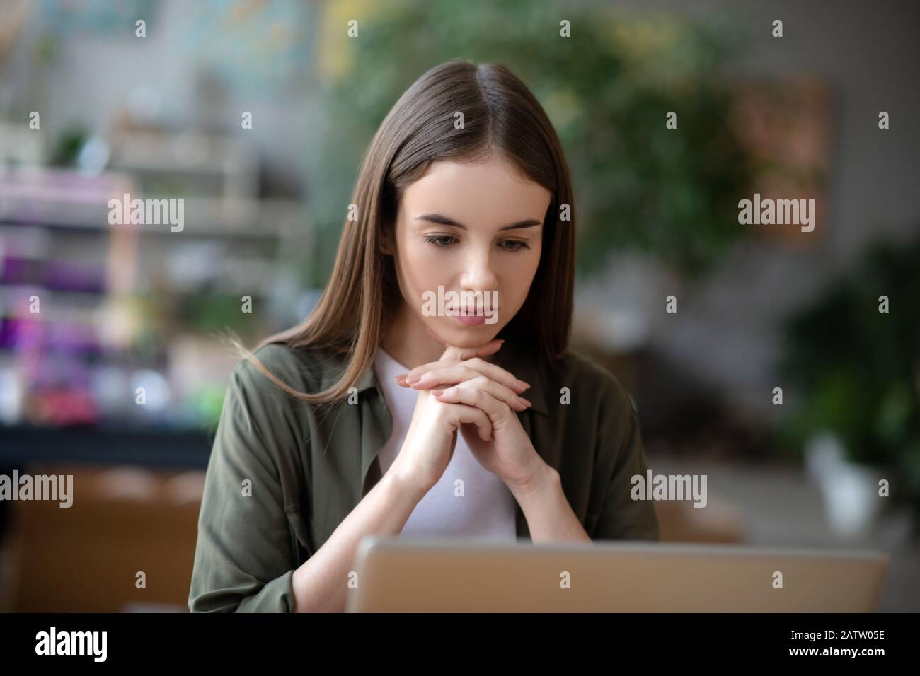 Fatigue. Young pretty girl in office in front of laptop holding hands in front of face looking tiredly at screen. Stock Photo