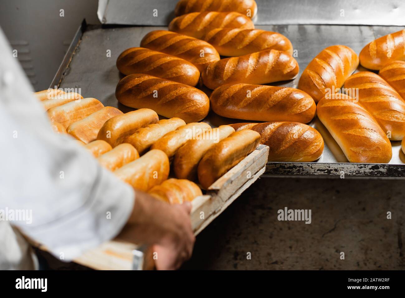 A baker in a bakery stacks fresh hot bread in a wooden crate