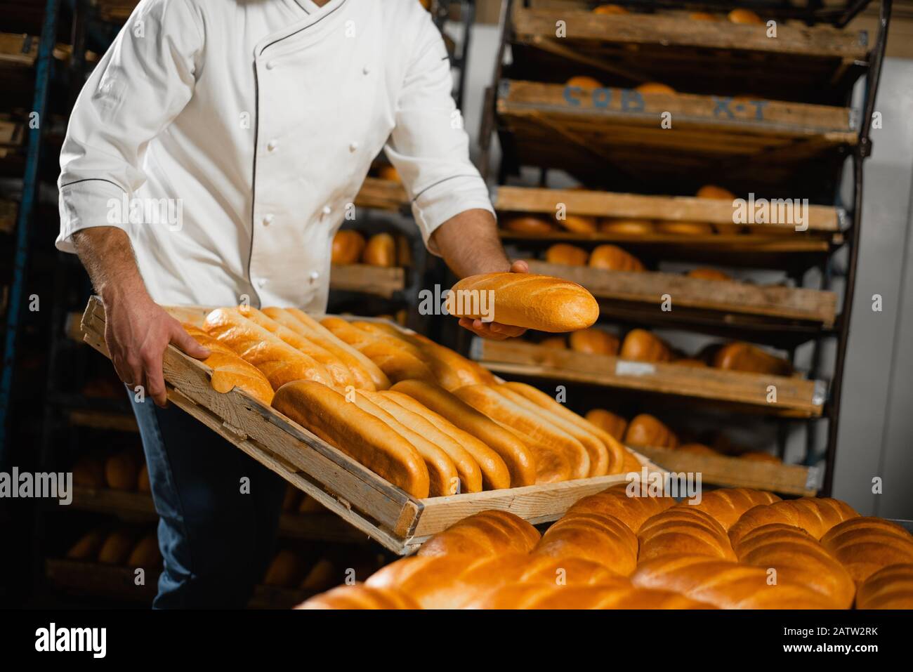 A baker in a bakery stacks fresh hot bread in a wooden crate