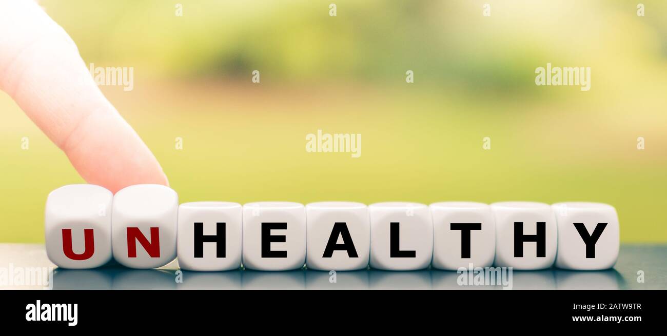 Hand turns dice and changes the word 'unhealthy' to 'healthy'. Stock Photo