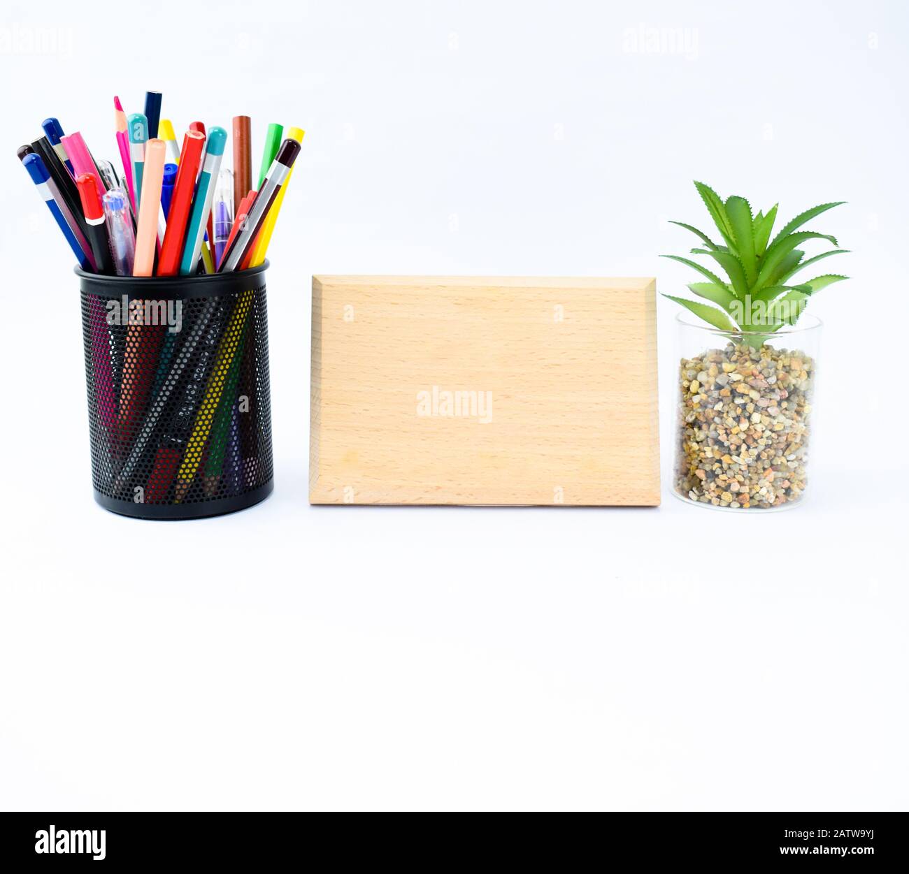 A empty wood plaque template along side a miniature tree and pencil holder full of different colored pencils Stock Photo