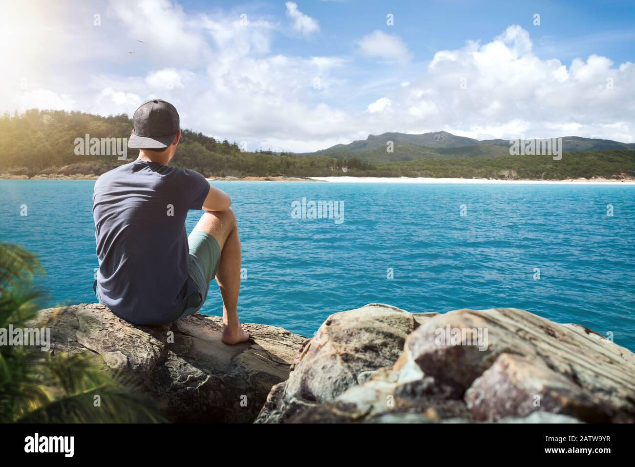 Young man sitting on a rock surrounded by tropical waters Stock Photo