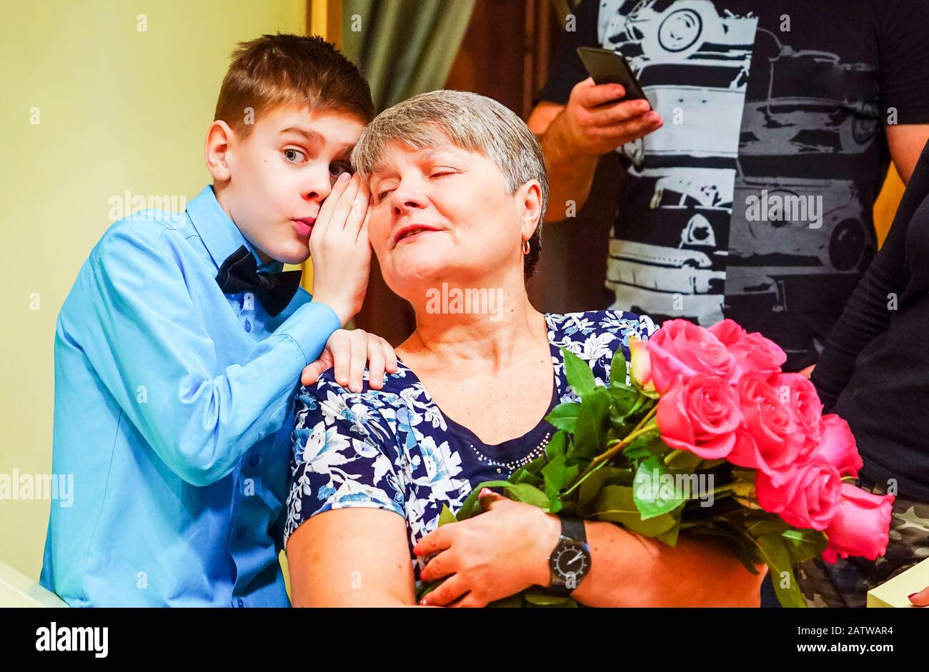 The boy whispers in his grandmother's ear and shares the news Stock Photo