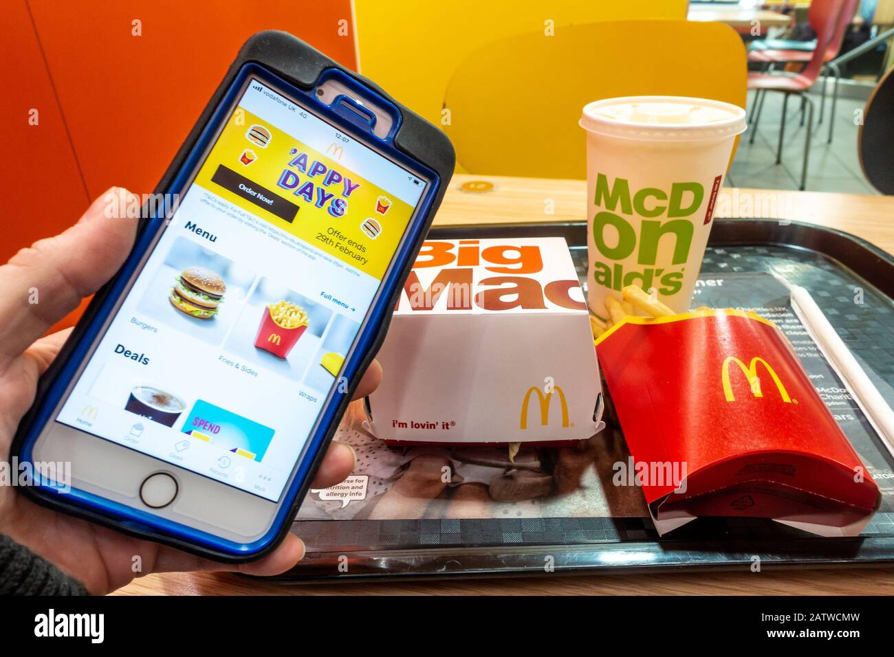 A hand holding a mobile phone with the McDonalds app in front of a a Big Mac meal in a <cDonalds fast food restaurant. Stock Photo