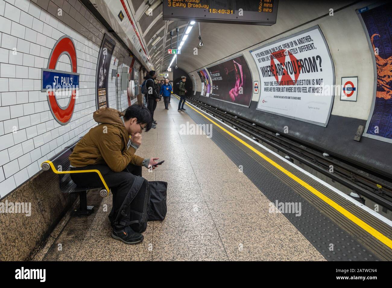 A man sits on a bench and uses his mobile phone as he waits for a train at St Paul's London Underground station. Stock Photo