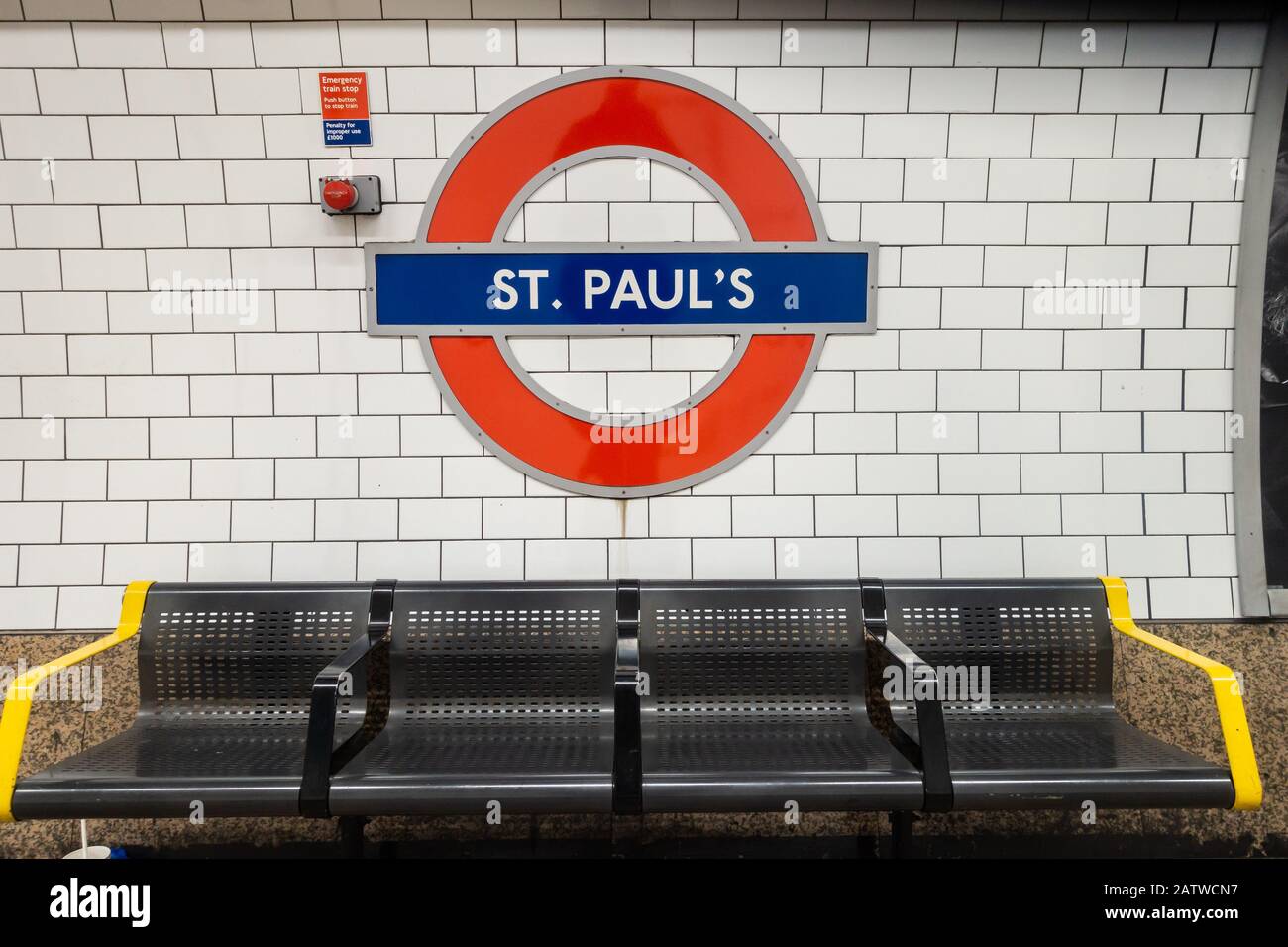 A London Underground symbol on the wall of St Paul's station above a row of seats. Stock Photo