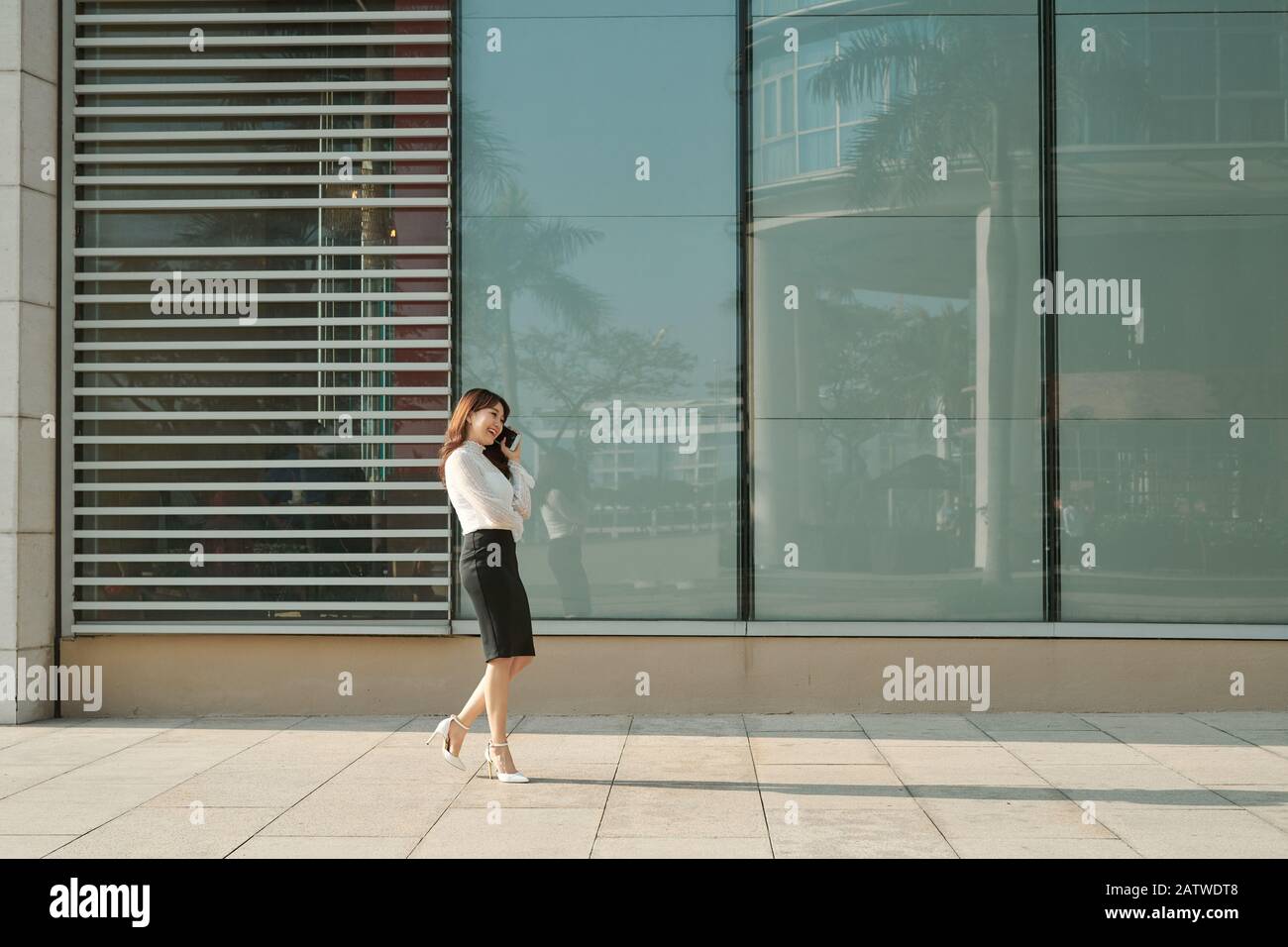 Beautiful female business woman walks in city park  and talking on cell phone Stock Photo