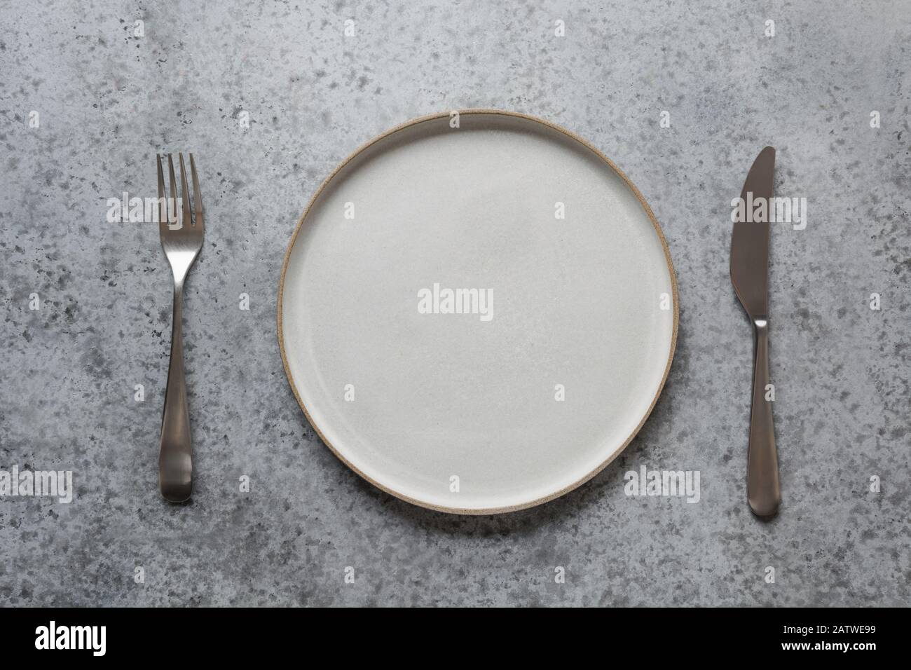 Empty modern modus plate, fork and knife on grey stone table. Minimal table place setting. Space for text or menu. View from above. Stock Photo