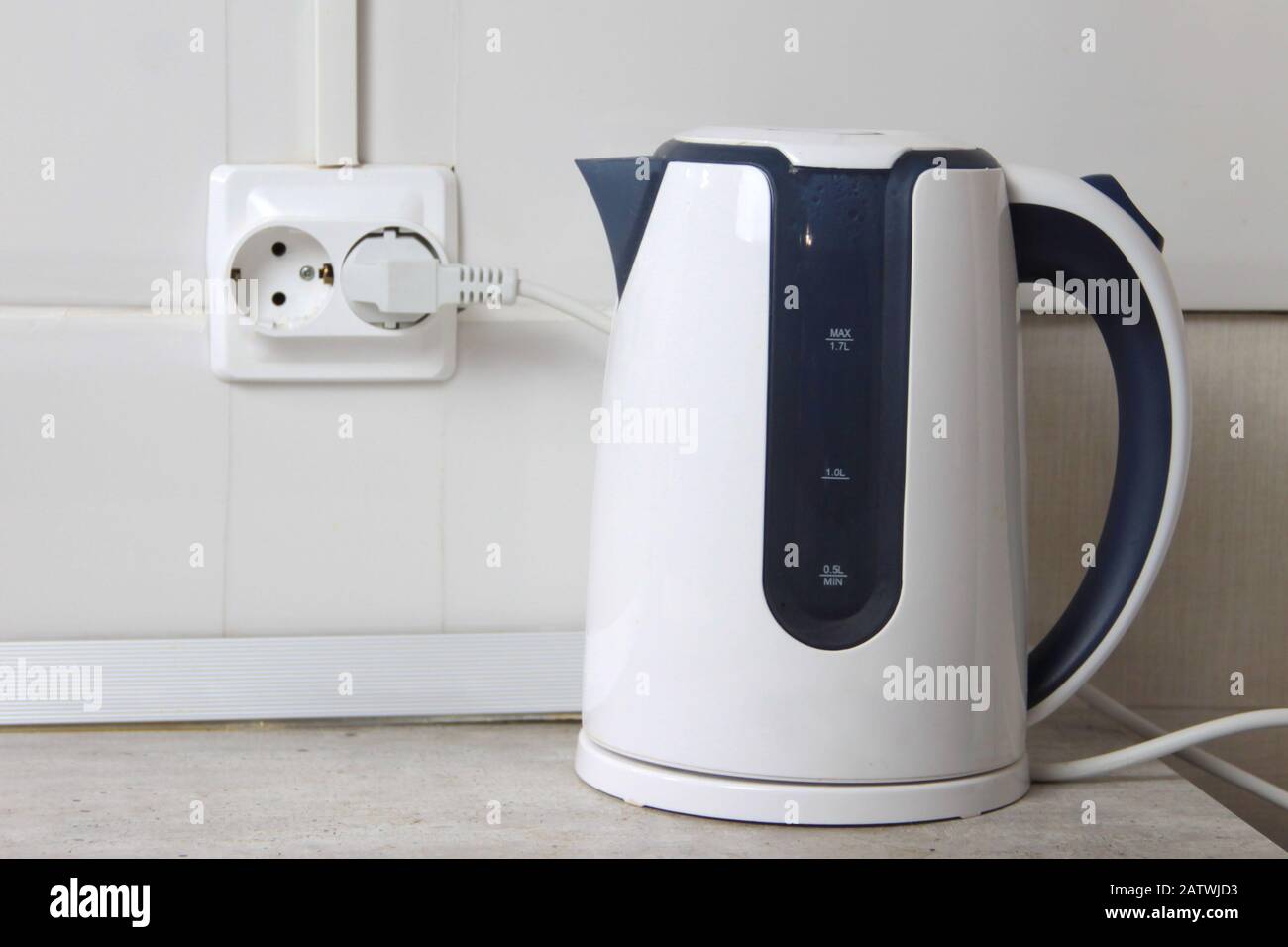 https://c8.alamy.com/comp/2ATWJD3/white-electric-kettle-stands-on-a-gray-table-plugged-into-a-power-outlet-2ATWJD3.jpg
