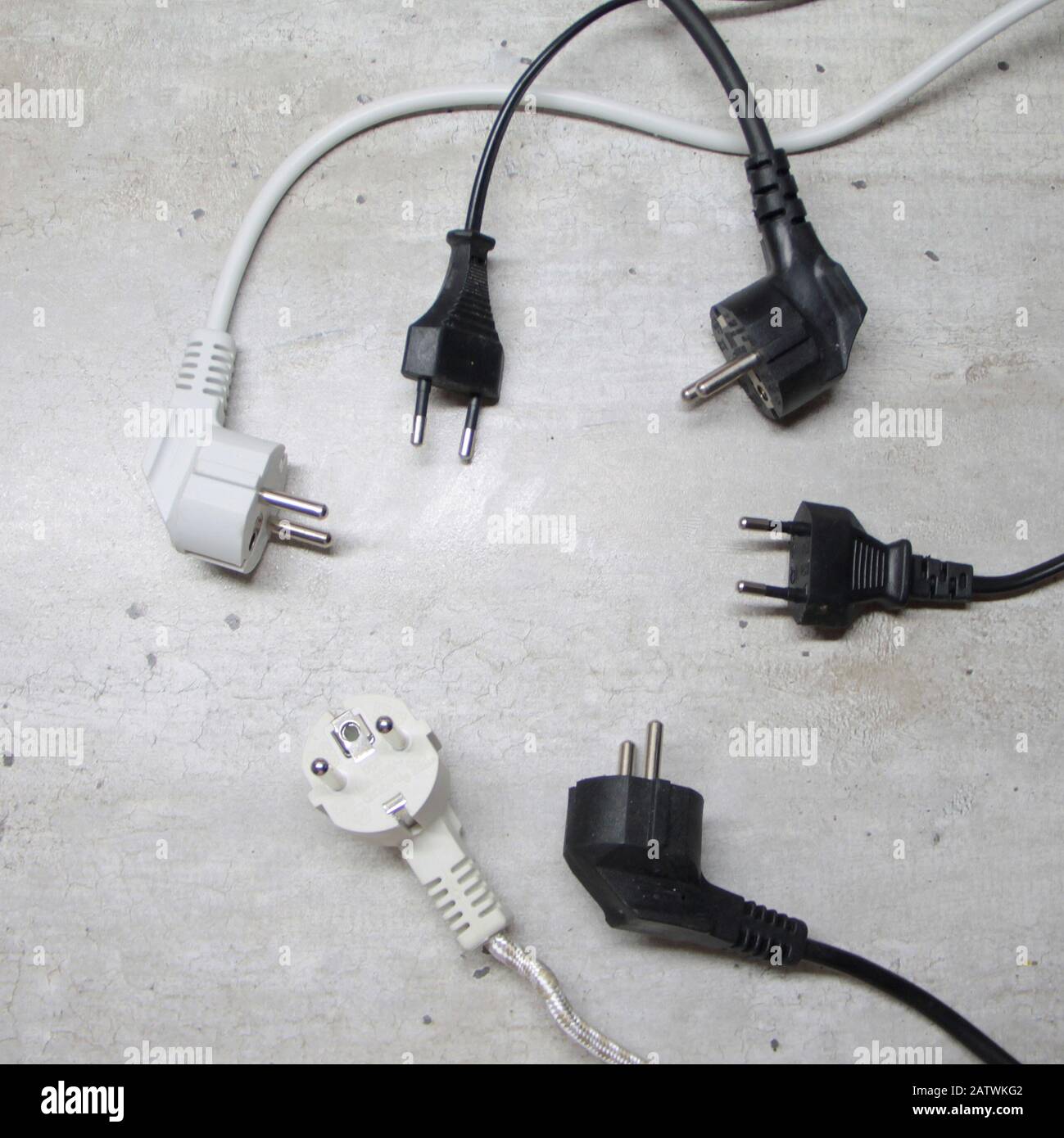 Electric plugs with cords lie on a gray surface in a circle. Stock Photo