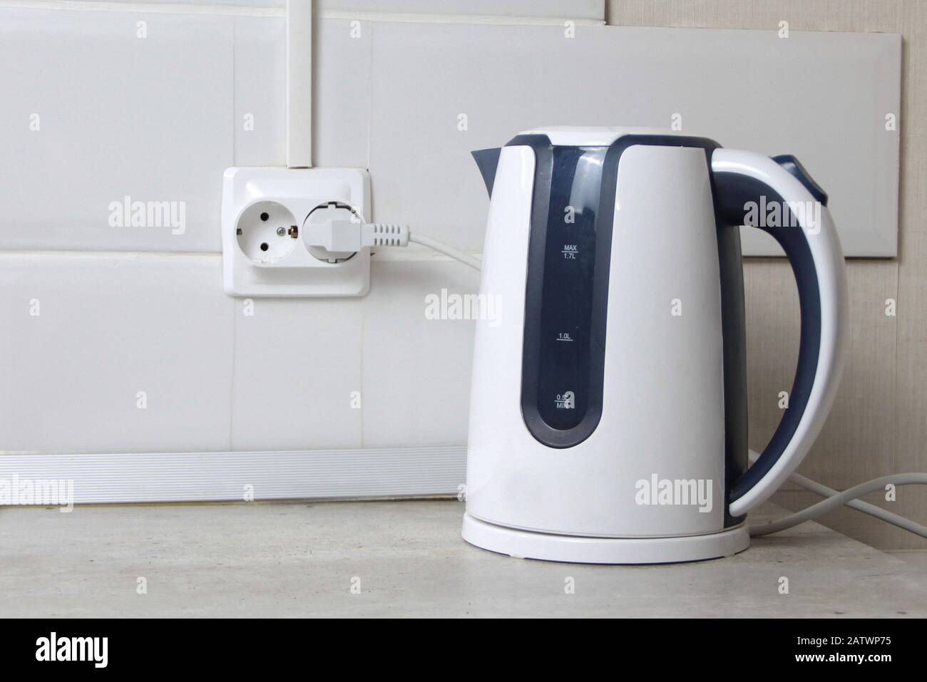 https://c8.alamy.com/comp/2ATWP75/white-electric-kettle-stands-on-a-gray-table-plugged-into-a-power-outlet-2ATWP75.jpg