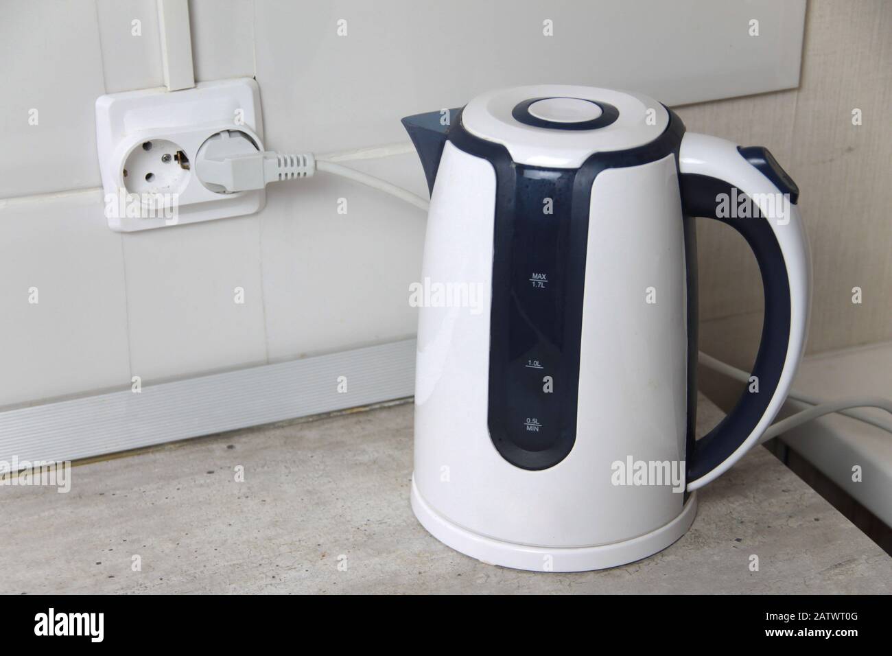 https://c8.alamy.com/comp/2ATWT0G/white-electric-kettle-stands-on-a-gray-table-plugged-into-a-power-outlet-2ATWT0G.jpg