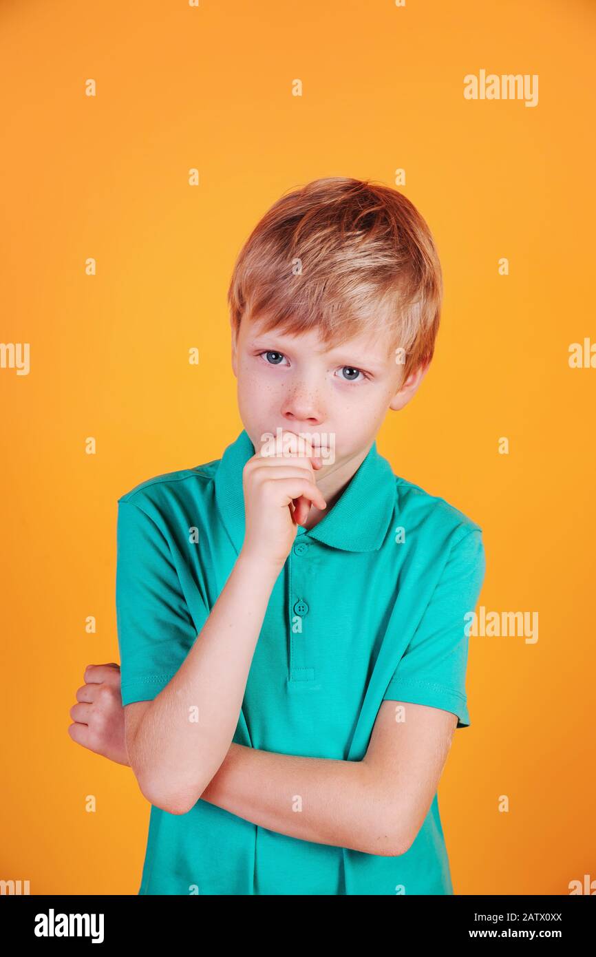 Thinking little boy child in turquoise t-shirt on yellow background. Stock Photo